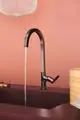 Küchenarmatur von Ideal Standard mit schwarzem, eckigem Auslauf und Wasserfluss. Sie ist an einem dunklen Waschbecken montiert, vor einem rosafarbenen Hintergrund.